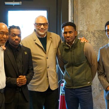 Five men posing indoors, smiling and dressed in semi-formal attire.