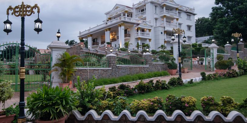 Elegant white mansion with lush garden and ornate lampposts.