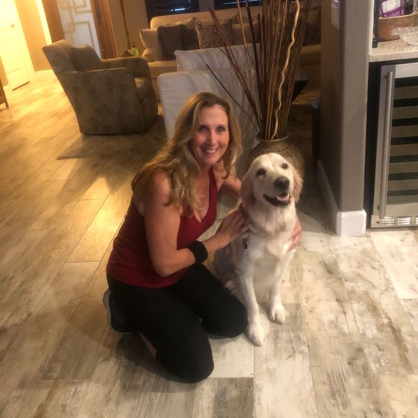Woman kneeling and smiling next to a happy golden retriever in a cozy living room.