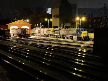 Model trains on illuminated tracks at night.