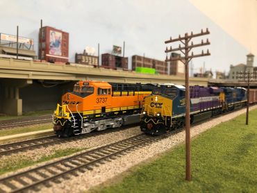 Model trains on tracks with a cityscape background.