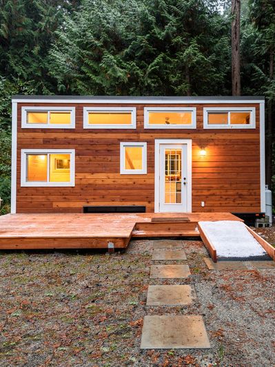 a tiny home in the middle a wooded area. the siding looks like natural wood and has a small deck