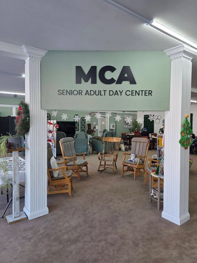Entrance to MCA Senior Adult Day Center with wooden rocking chairs inside.