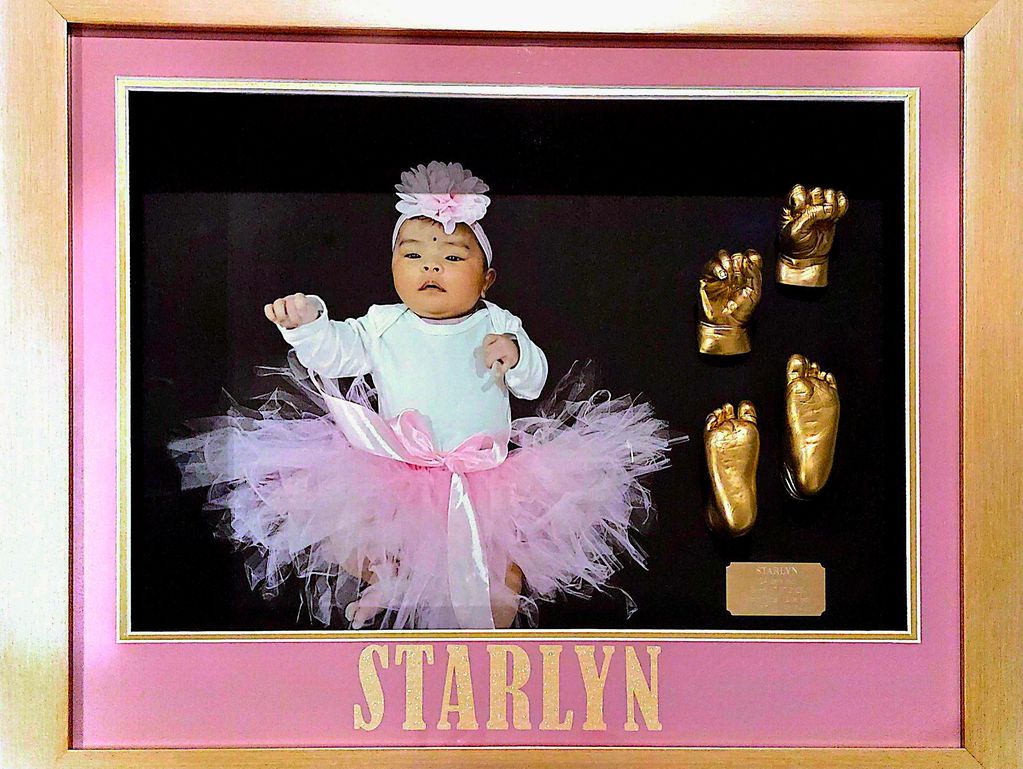 Framed baby photo with pink tutu and gold hand and foot casts labeled 'Starlyn'.