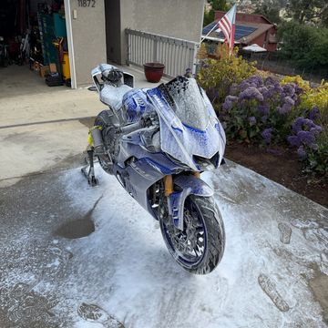 A blue Yamaha motorcycle covered in soap suds being washed outside a house.