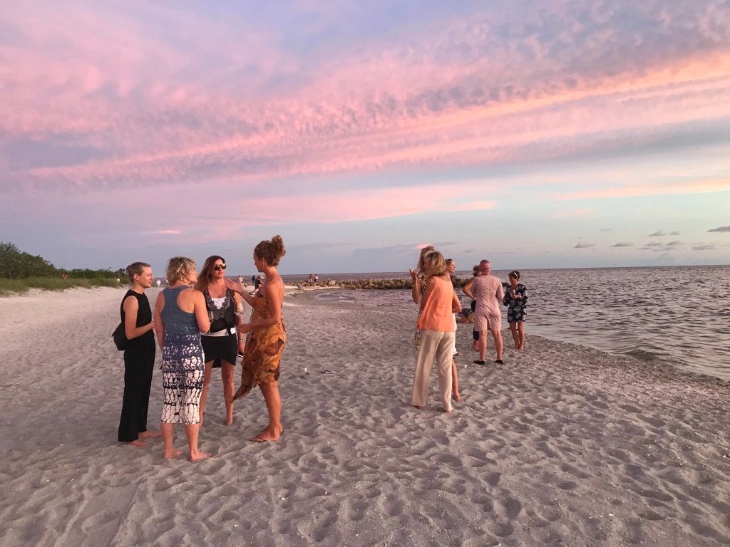 Groups of people socializing on a sandy beach at sunset.