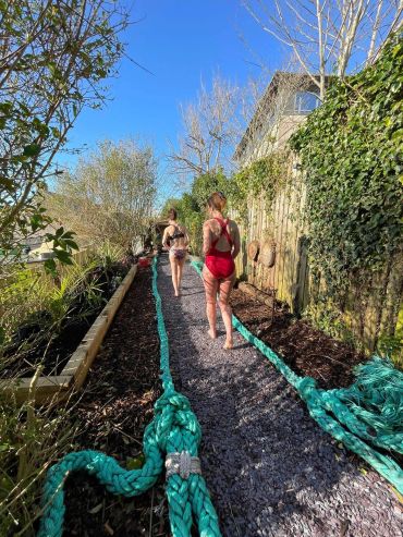 Two girls walking on a gravel path with thick green ropes.