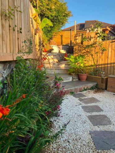 Garden path with plants and stairs in sunlight.
