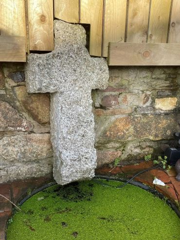 Stone cross hanging above green water.