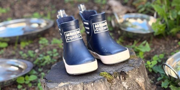 A pair of navy blue children's rain boots on a tree stump outdoors.