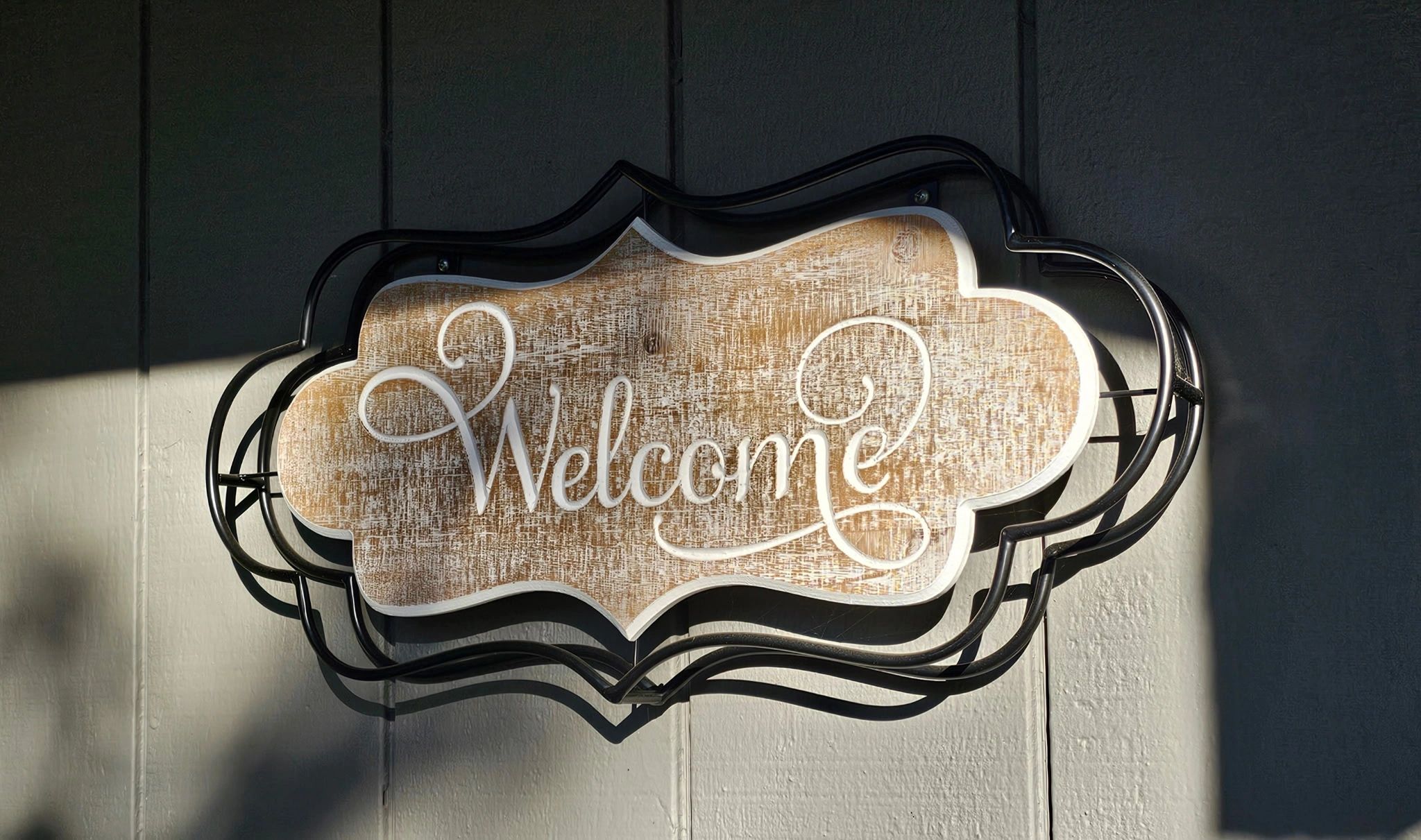 Rustic wooden welcome sign with decorative metal frame on a textured wall.