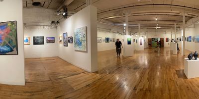 Spacious art gallery with paintings displayed on white walls and wooden floors.