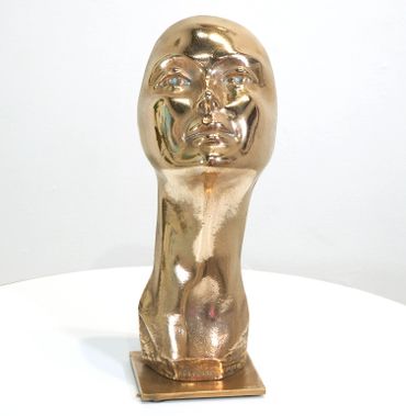Golden abstract sculpture of a human head and neck on a square base.