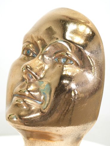 Close-up of a shiny golden face sculpture with reflective features.