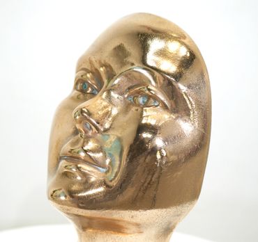 Close-up of a shiny golden face sculpture with reflective features.