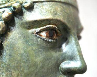 Close-up of an ancient bronze statue's eye and nose with detailed craftsmanship.