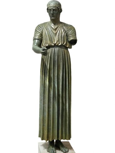 Ancient bronze statue of a standing male figure with detailed drapery and missing arm.