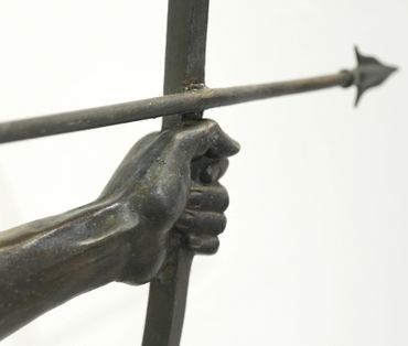 Bronze sculpture of a hand gripping a bow with an arrow drawn.