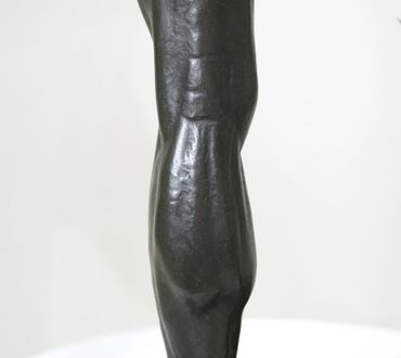 Close-up of a dark bronze muscular sculpture with defined anatomy.