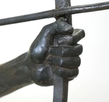 Close-up of a bronze hand gripping a sword hilt in a sculpture.