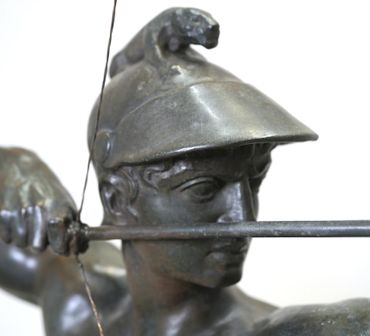 Close-up of a bronze statue of an archer wearing a helmet.