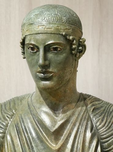 Ancient bronze statue of a man with detailed facial features and robe.