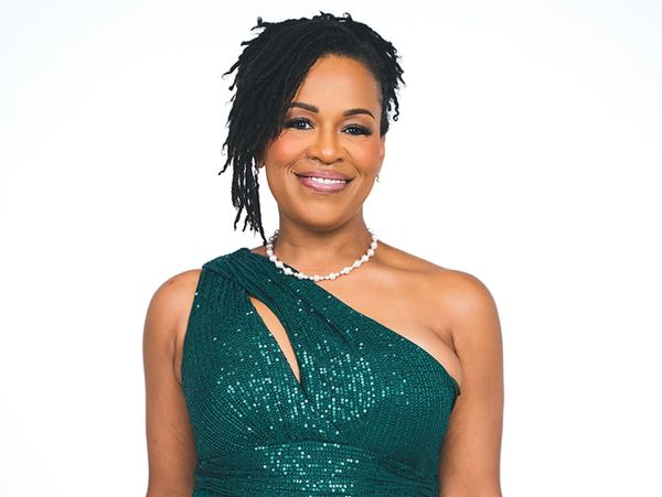Woman in a sparkling green one-shoulder gown smiling against a white background.