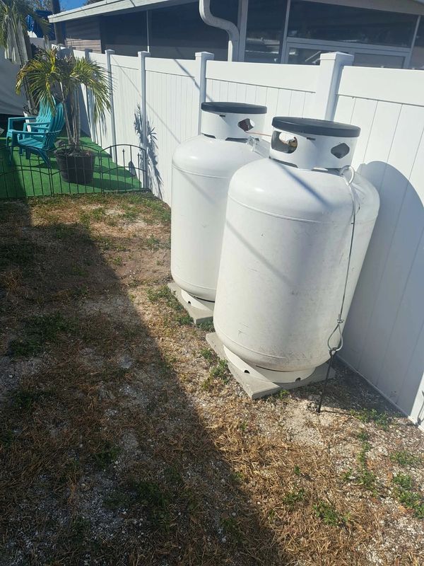 Two large white propane tanks secured by a fence in a backyard.