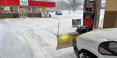 Snowplow attached to a truck clearing snow at a gas station.