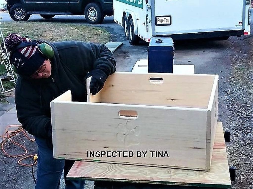 A woman inspecting the sanding on a custom-built wooden whelping box for Shih Tzu puppies.