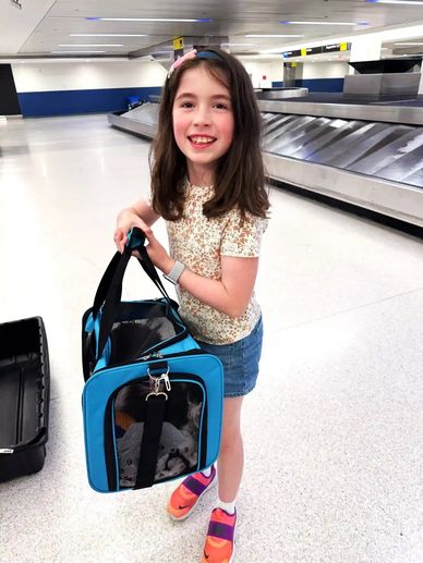 A little girl in the New Jersey EWR Airport holding her new Shih Tzu puppy in an airline carrier.