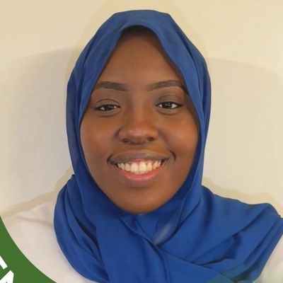 Smiling woman wearing a blue hijab against a plain background.