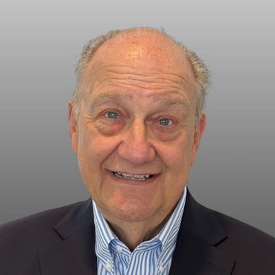 Smiling elderly man in a suit with a gray background.