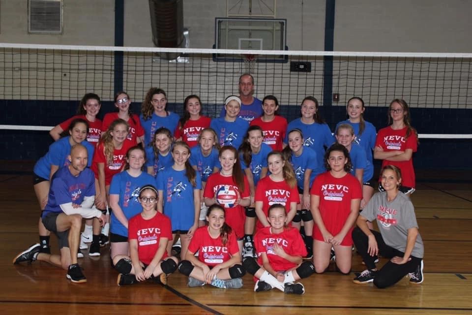 Youth volleyball team posing together in gym with coaches.