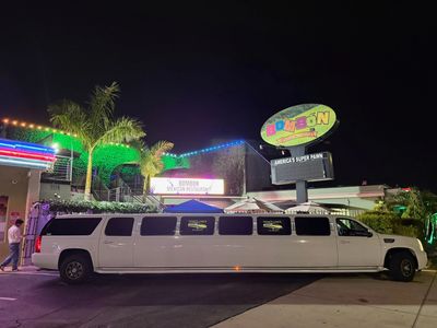 A long white limousine parked outside a neon-lit building at night.