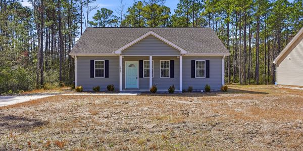 A small gray house with a blue door set in a dry yard surrounded by trees.