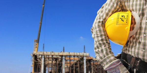 Construction worker holding a yellow safety helmet at a building site.