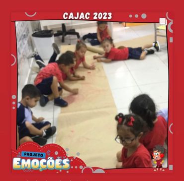 Children in red shirts drawing on a large paper on the floor during CAJAC 2023 project.