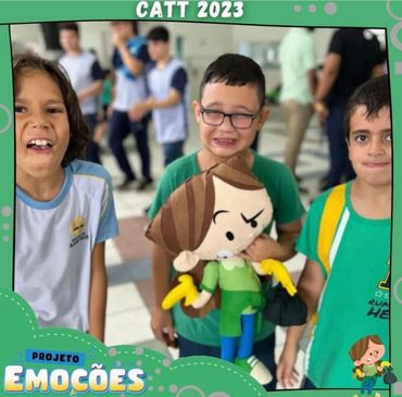 Three boys smiling and holding a cartoonish doll at a school event.