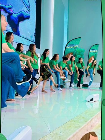 Group of people in green shirts performing a coordinated leg movement on stage.