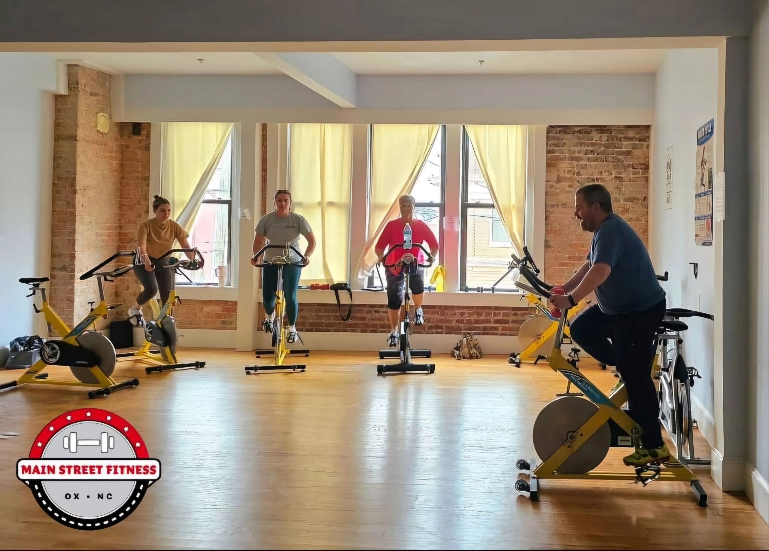 Spin Class in a well lit room with windows and people on stationary bikes.