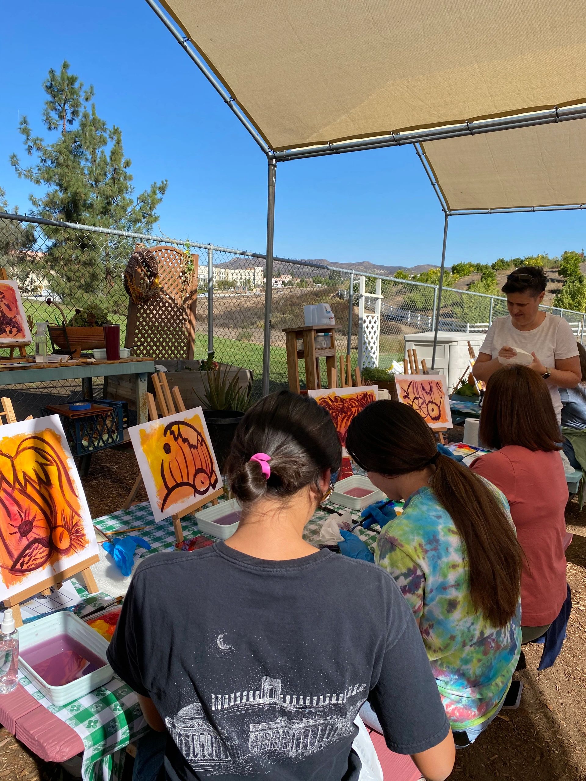 People participating in an outdoor painting class under a canopy.