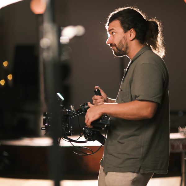 Man operating professional video camera in a dimly lit room.