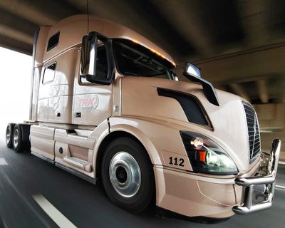 A beige semi-truck driving on a road.
