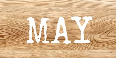 The word 'MAY' written in white on a wooden background.
