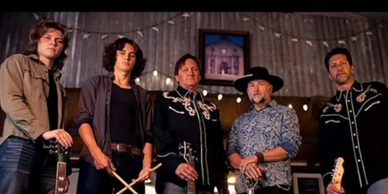 A band of five men posing with musical instruments and drumsticks against a festive backdrop.