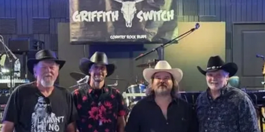 Four men in cowboy hats posing in front of a band stage.