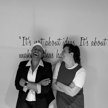 Two women laughing together in front of an inspirational quote on a wall.