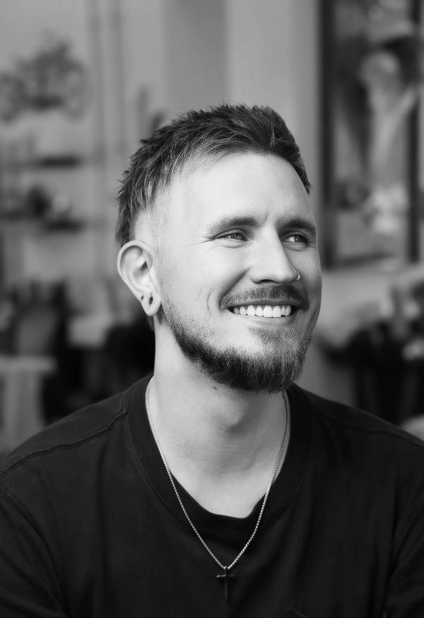 Smiling young man with a beard and a necklace in a black shirt.