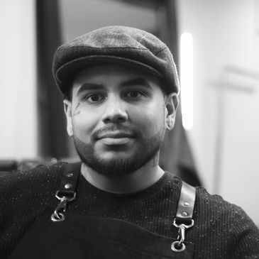 Man wearing a flat cap and apron, looking at the camera.
